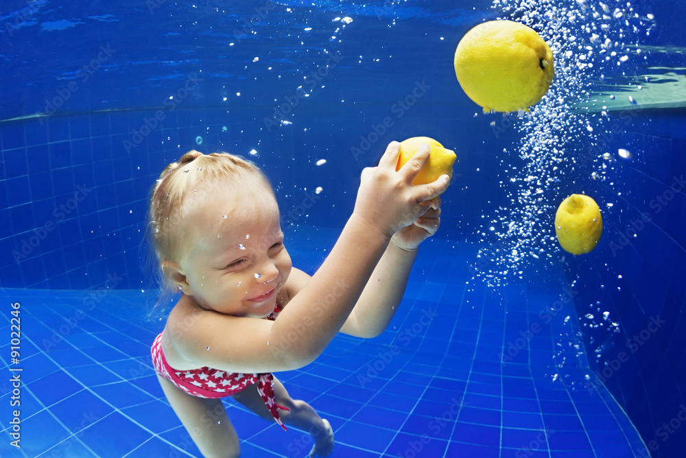 儿童游泳课-小女婴在游泳池里跳到水下，享受柠檬油炸的乐趣