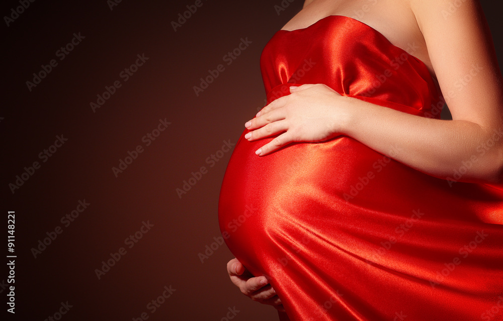 身穿红色丝绸连衣裙的孕妇腹部翻腾
