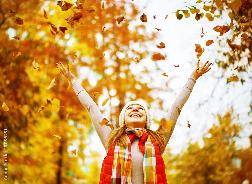 Happy girl throws up autumn leaves in park for walk outdoors
