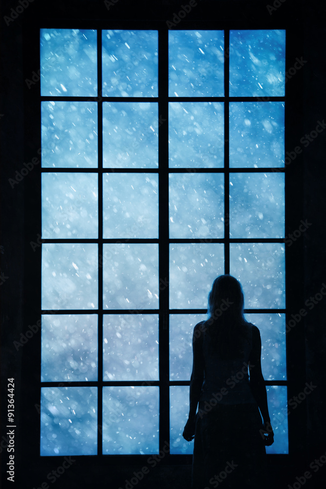 孤独的女人站着，透过紧闭的大玻璃窗看着可爱的雪，想着ab