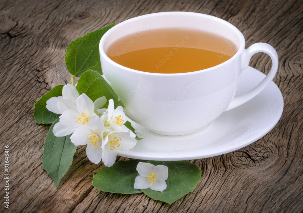 Cup of green tea with jasmine flowers on wooden background
