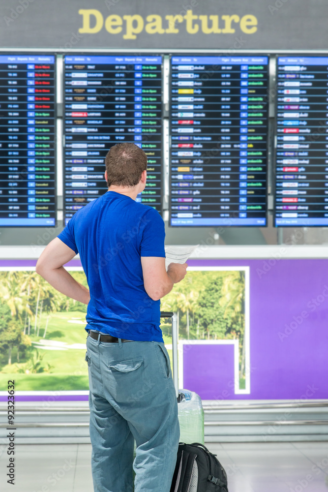 一名背着背包的年轻人在机场接近航班时刻表