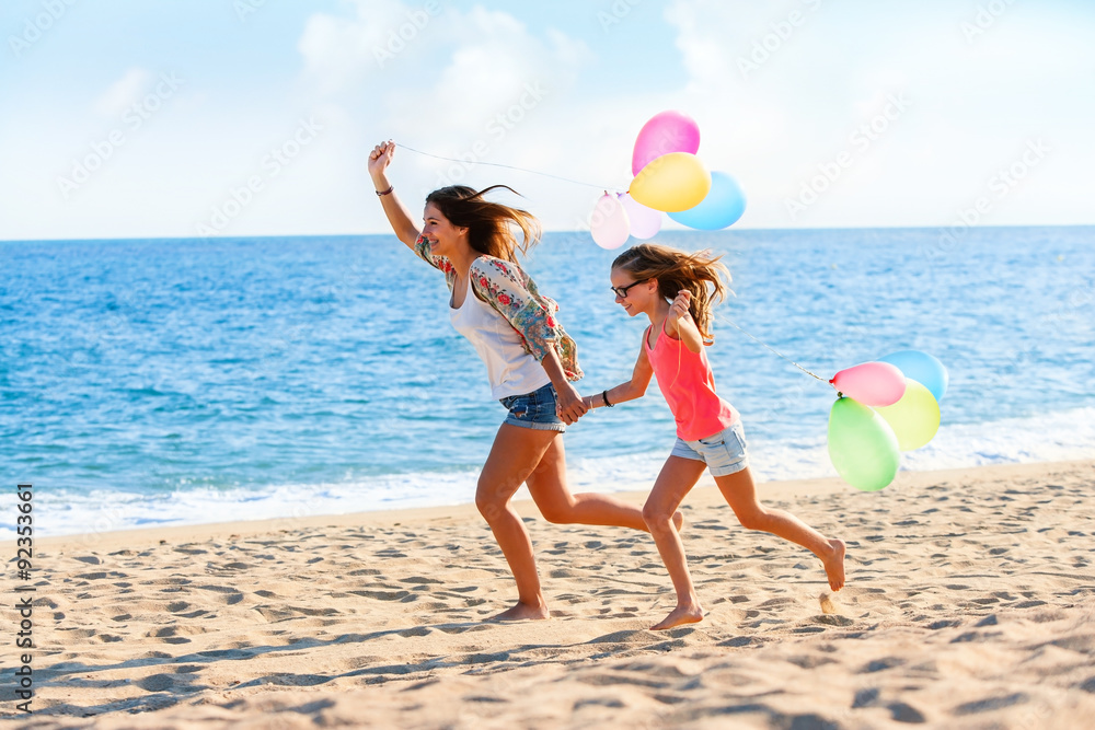 Young girls running with balloons on beach.