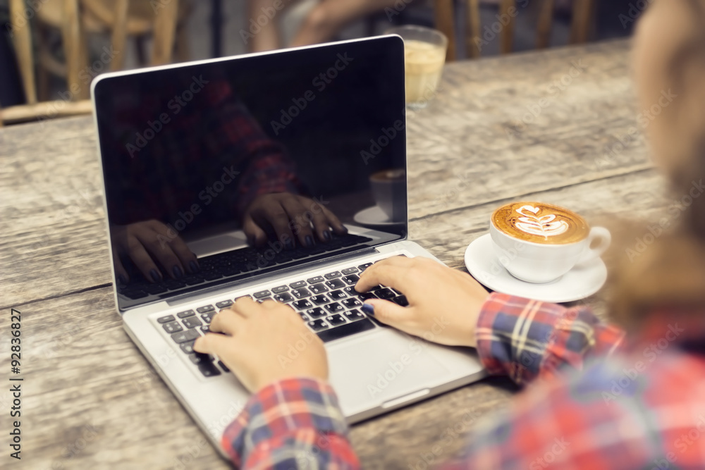 木桌上的时髦女孩手、笔记本电脑和咖啡杯