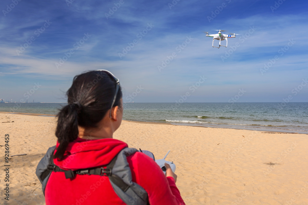 Woman flying a drone quadrocopter at the sea