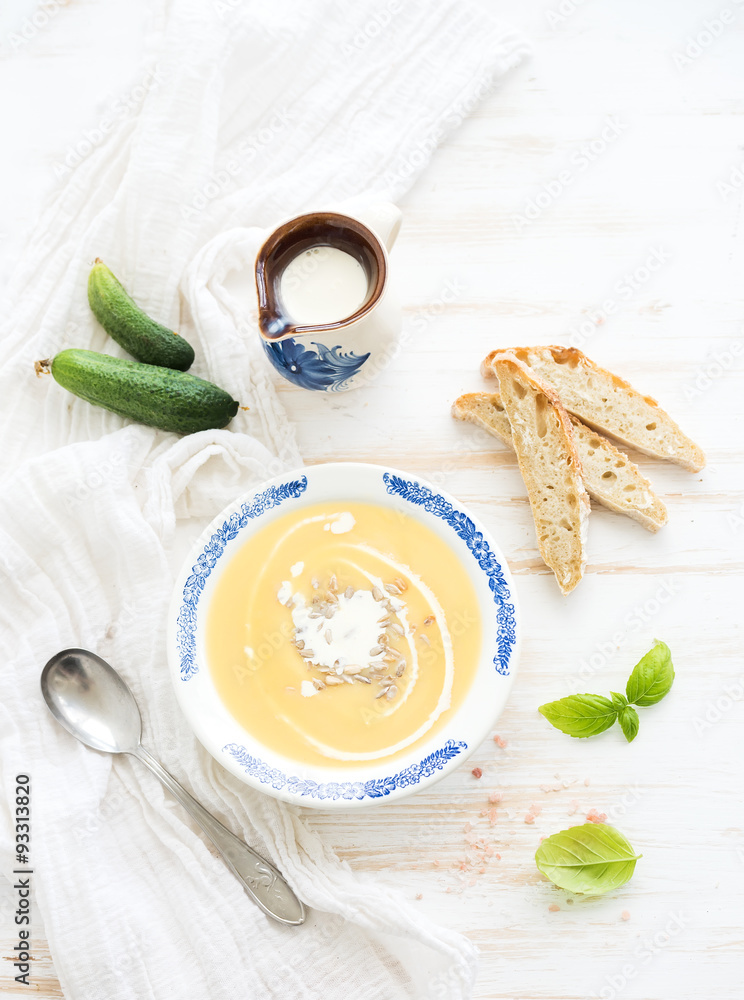 Pumpkin soup with cream, fresh basil, cucumbers and bread in