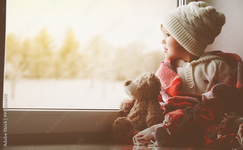 child little girl with  teddy bear at window and looking at wint
