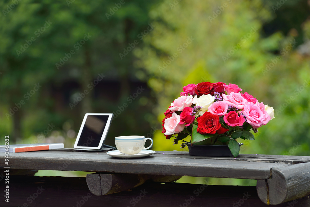公园咖啡馆咖啡桌上放着平板电脑和鲜花的咖啡杯