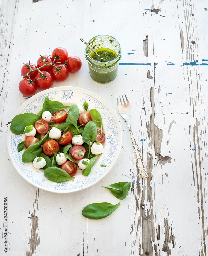 Caprese salad, homemade pesto sauce. Cherry-tomatoes, baby spinach and mozzarella in ceramic plate o