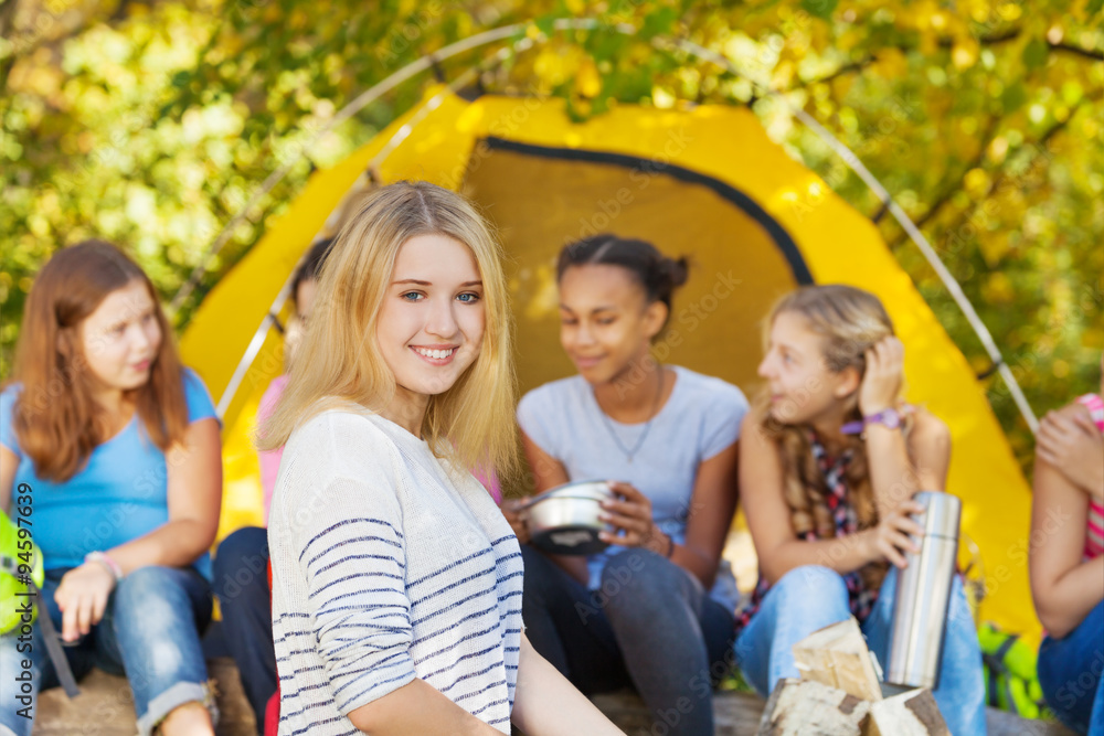 快乐美丽的女孩和朋友坐在帐篷附近