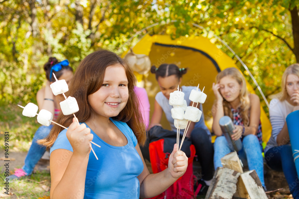 Girl holds sticks with marshmallow near tent