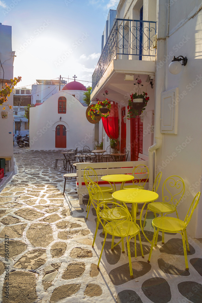 日出时的米科诺斯街景，配有小教堂和黄色桌椅，希腊