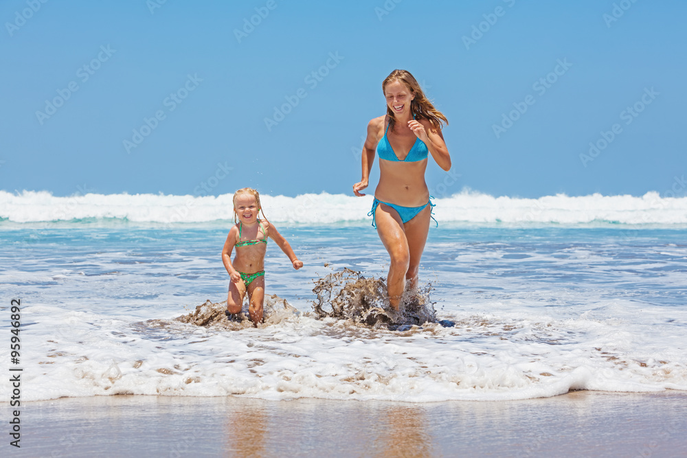 幸福的家庭——母亲和年幼的女儿在海浪中尽情游泳，奔跑时溅起水花。