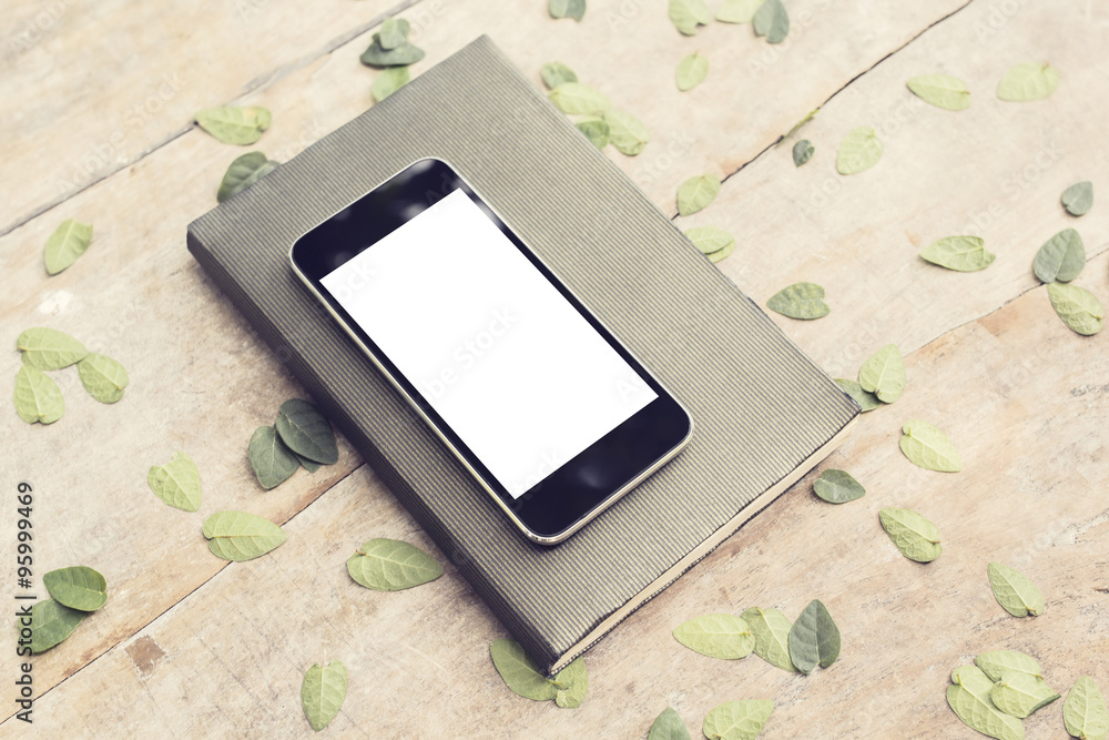 空白智能手机屏幕，带叶子的木桌上有日记，