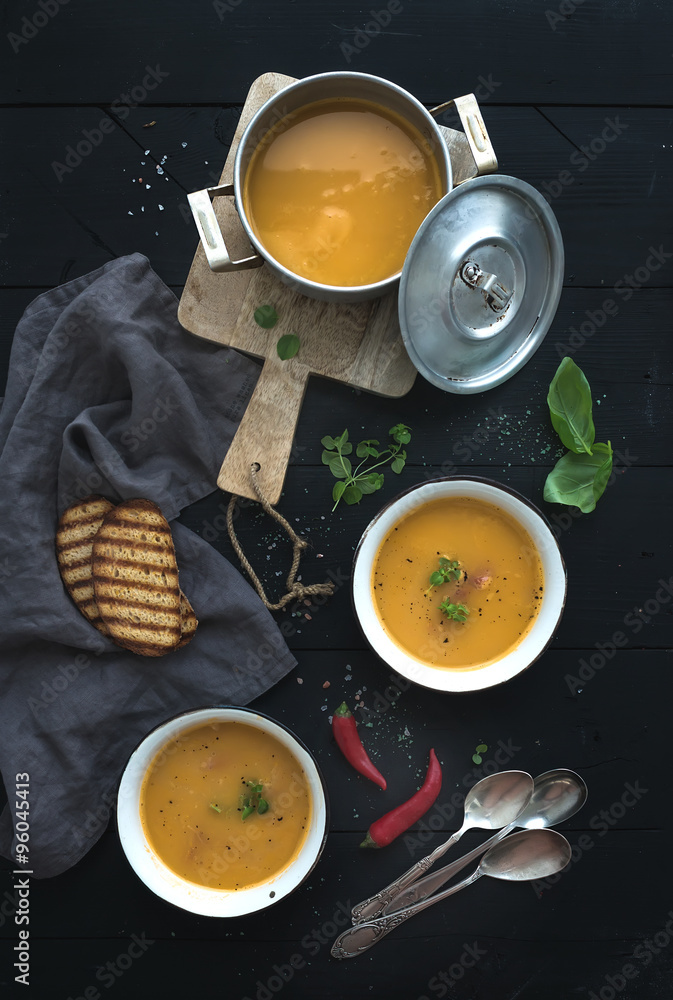 Red lentil soup with spices, herbs, bread in a rustic metal saucepan and bowls, over dark wood backd