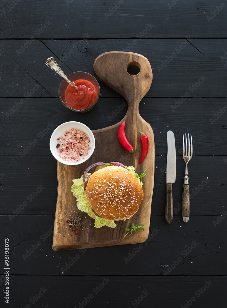 Fresh homemade burger on dark serving board with spicy tomato sauce, sea salt over black wooden back