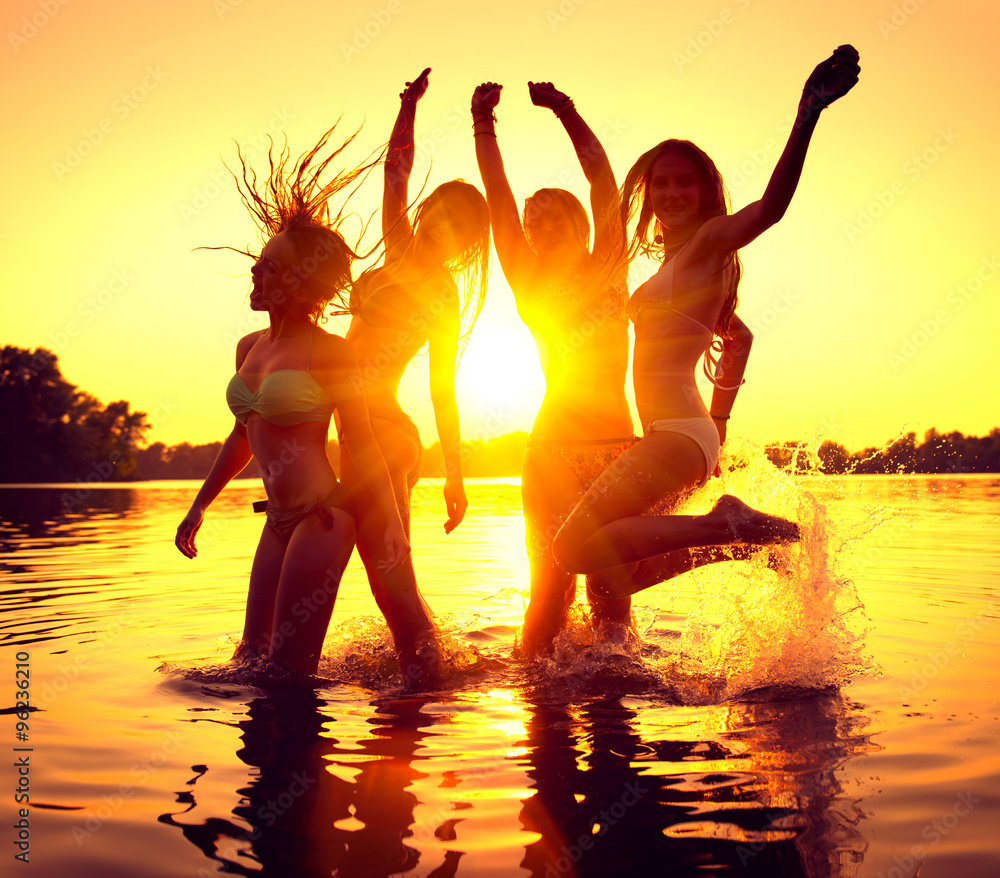 海滩派对。一群快乐的女孩在美丽的夏日日落下在水中跳舞。