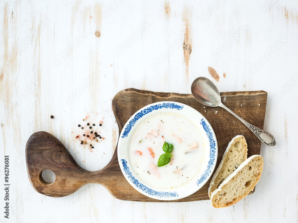 Scandinavian salmon soup with cream, fresh basil and bread in vintage ceramic plate on wooden servin