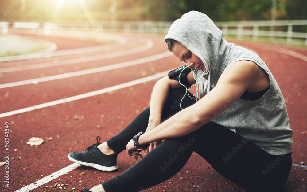 Young woman sitting on track field and preparing before running