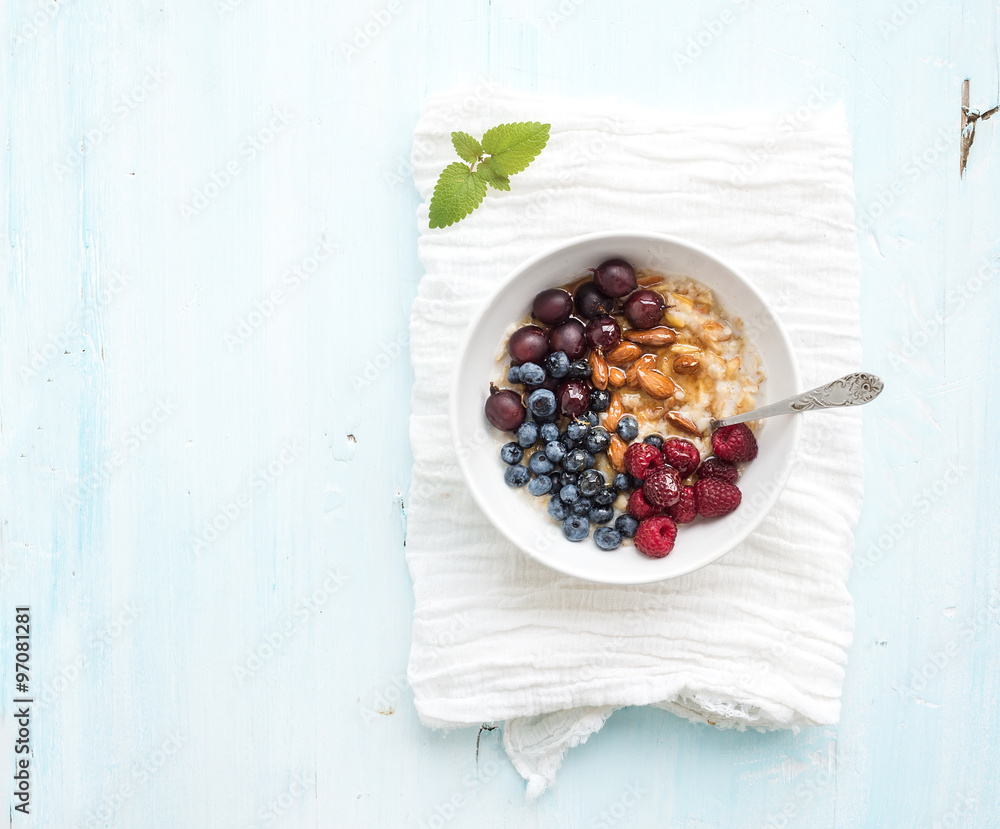 健康早餐套装。一碗燕麦粥，白餐巾上放着新鲜浆果、杏仁和蜂蜜。