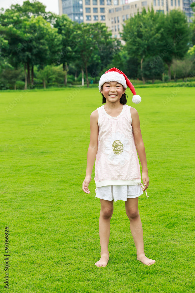 快乐的东方小女孩在草地上戴着圣诞帽