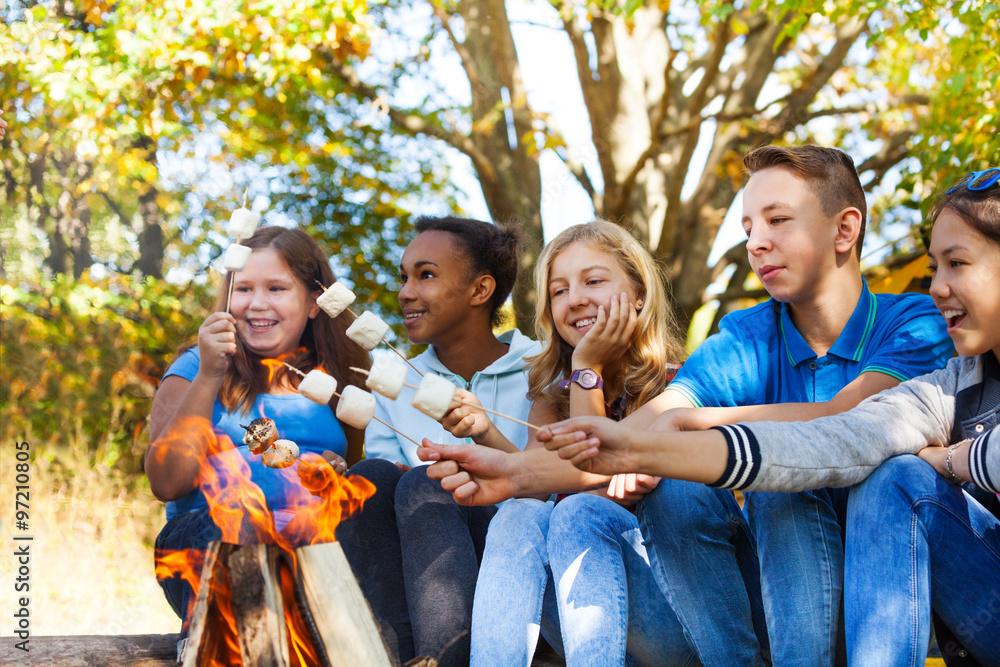 Group of teens hold marshmallow sticks near flame