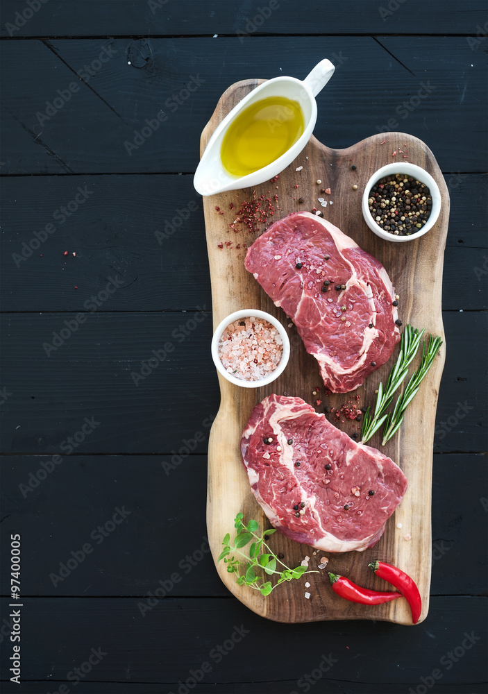 深色木质背景下砧板上的生鲜肉肋眼牛排主菜和调味料