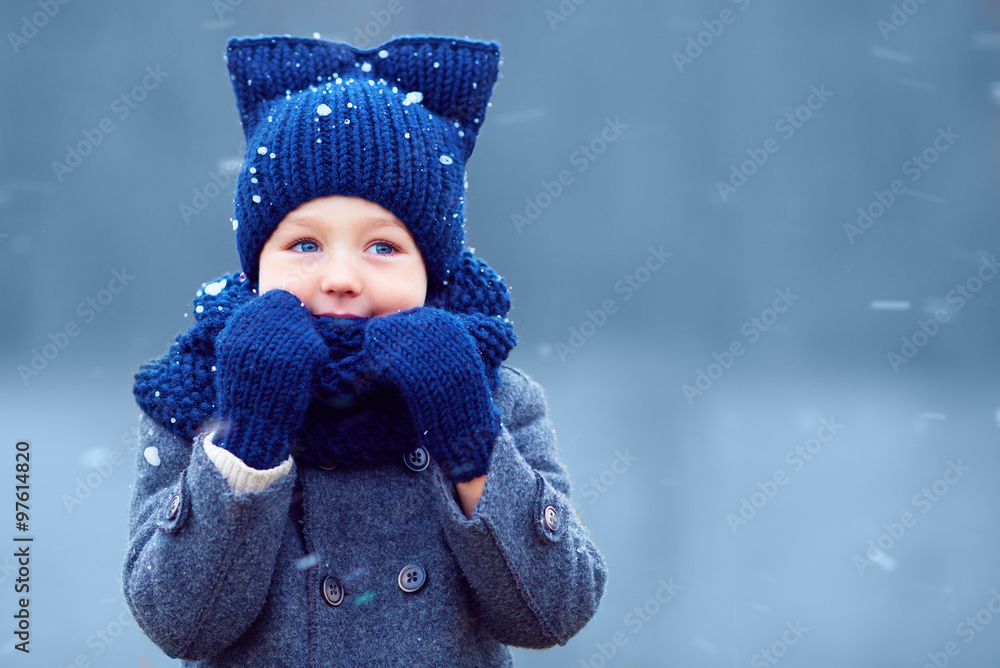 cute little boy, kid in winter clothes walking under the snow