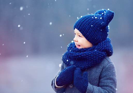 cute kid, boy in winter clothes playing under the snow