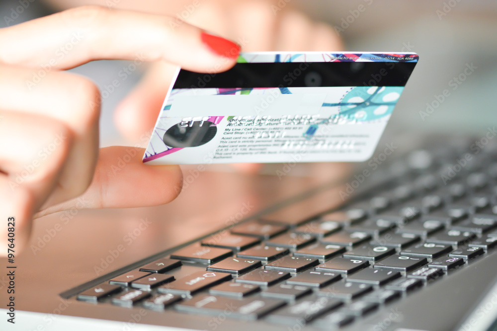 女子手持蓝色信用卡使用笔记本电脑进行网上购物的特写