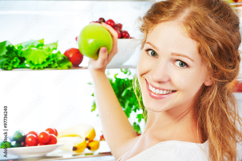 快乐的女人有苹果，打开的冰箱里有水果和蔬菜