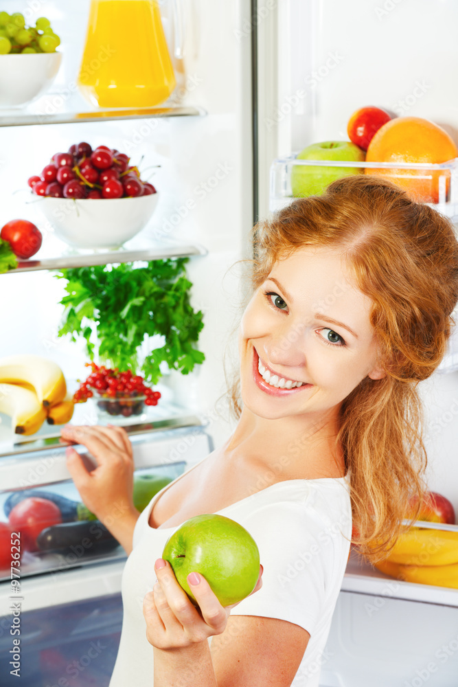 快乐的女人有苹果，打开的冰箱里有水果和蔬菜
