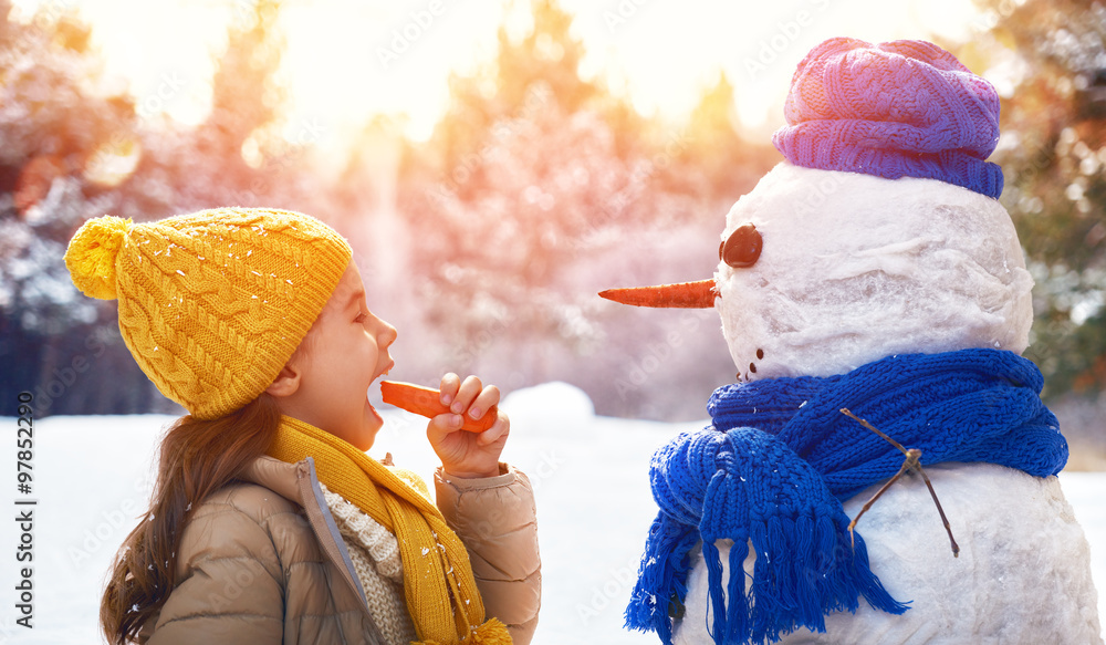 快乐的小女孩和雪人在雪地里散步
