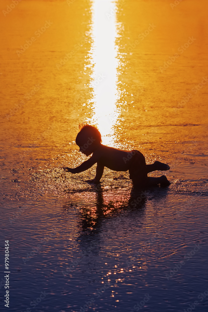 顽皮婴儿在潮湿的金色日落沙滩上奔跑，在海浪中游泳的黑影剪影