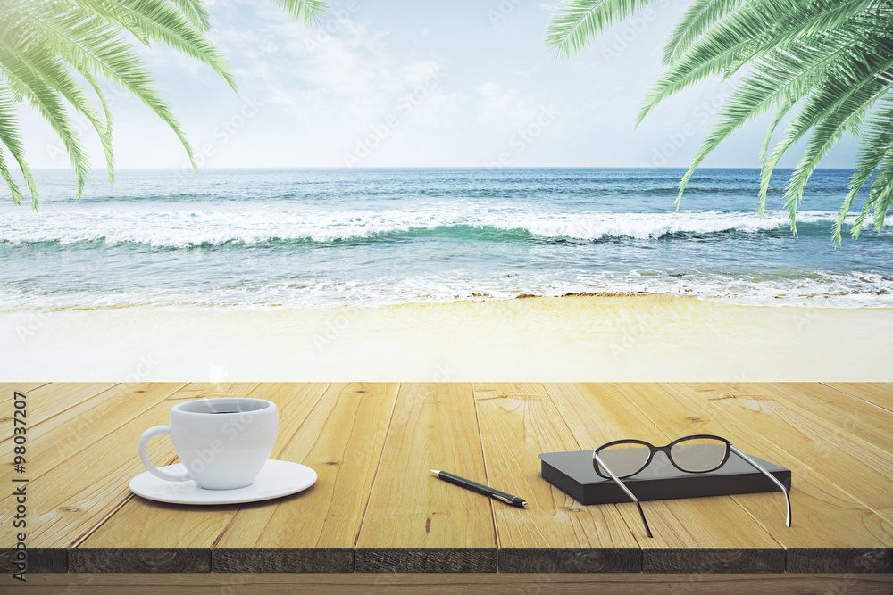 Wooden table with cup of coffee, eyeglasses and diary on the bea