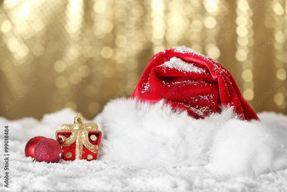 圣诞老人红帽子，金色背景下的人造雪上有圣诞装饰，clo