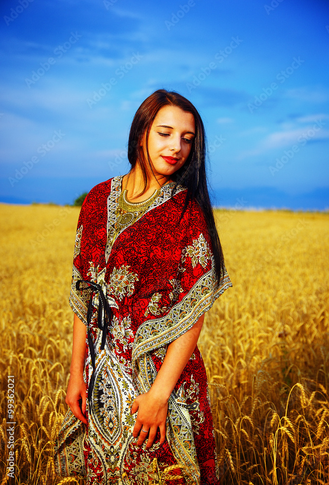 Smiling Young woman with ornamental dress standing on a wheat field with sunset. Natural background.