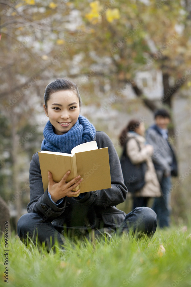 一个年轻女人坐在草地上看书，背景是人