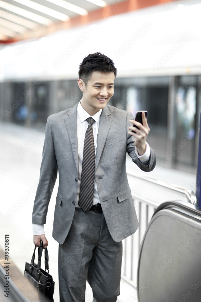 Happy businessman with smart phone on subway escalator
