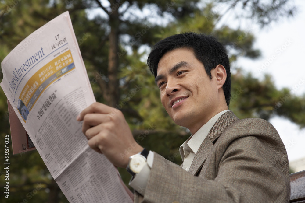 Businessman Sitting On A Park Bench Reading The Newspaper