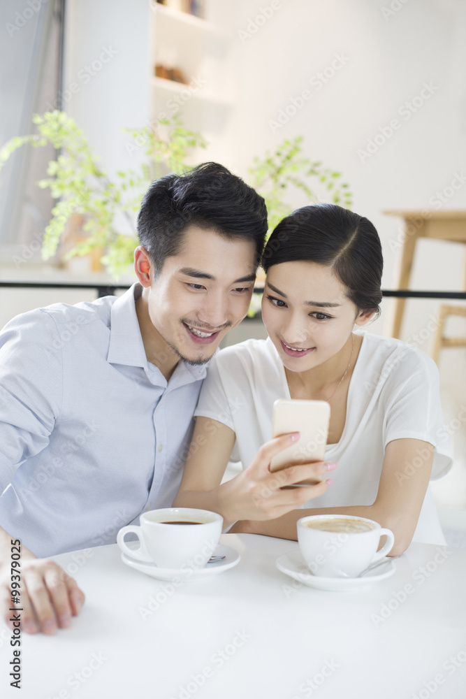 幸福的年轻夫妇在咖啡馆使用智能手机