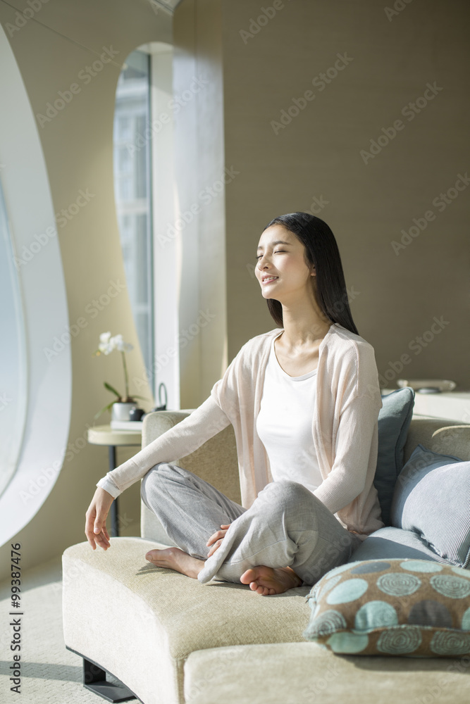 Happy young woman sitting on sofa with eyes closed