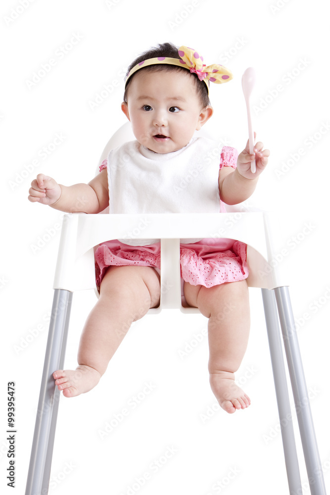 在婴儿高脚椅上拿着勺子的可爱女婴