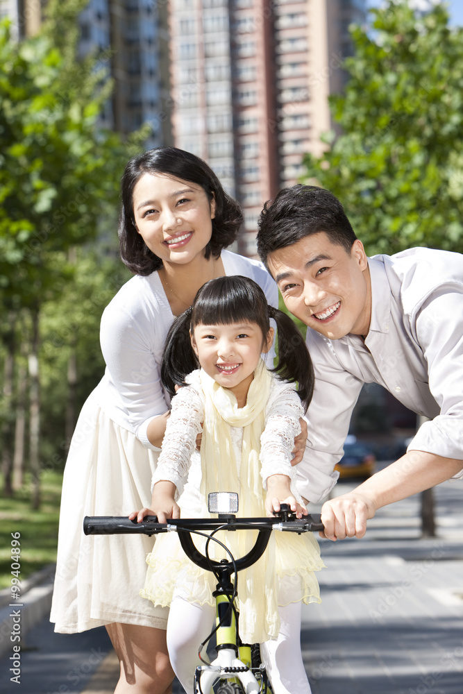 快乐的父母在街上教女儿骑自行车