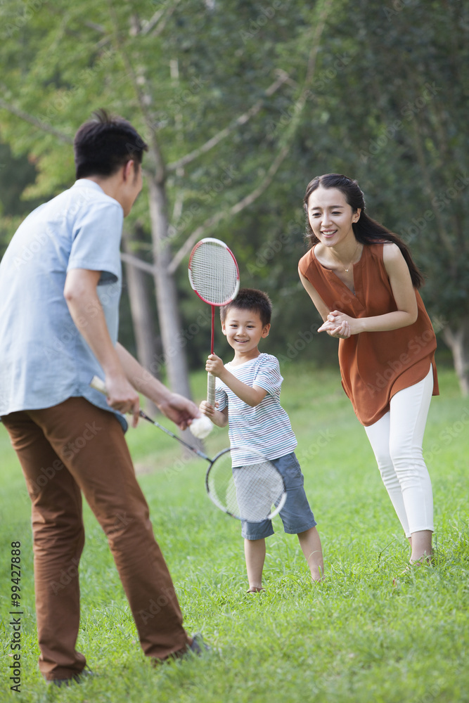 Happy young parents teaching son playing badminton
