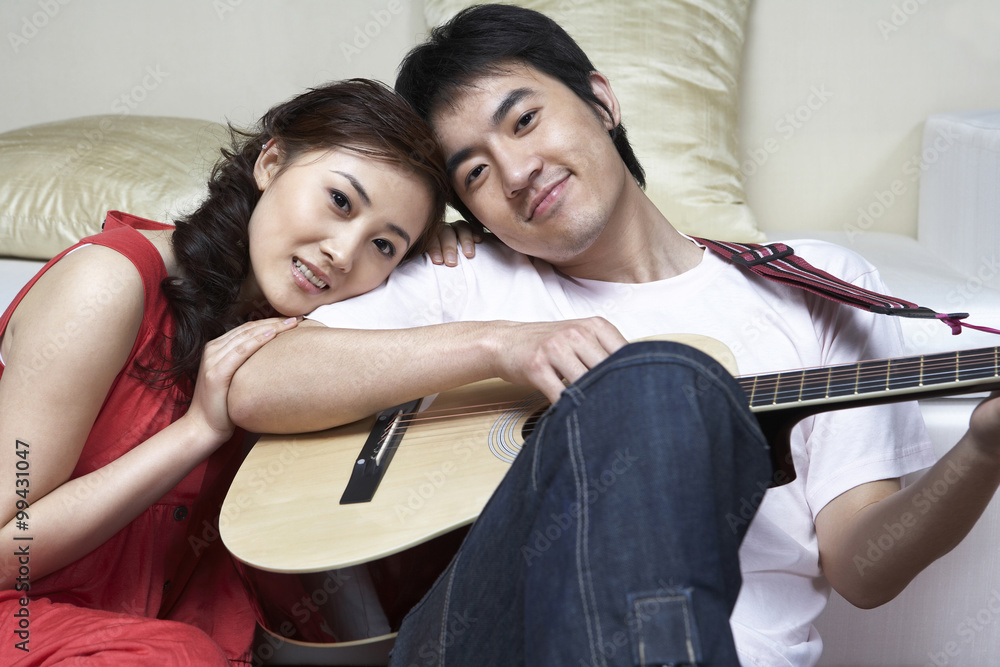 亚洲情侣深情地坐着，手里拿着吉他