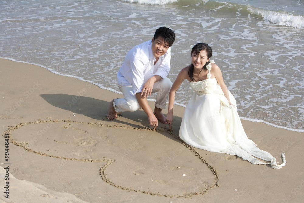 幸福的新婚夫妇在海滩上画心形