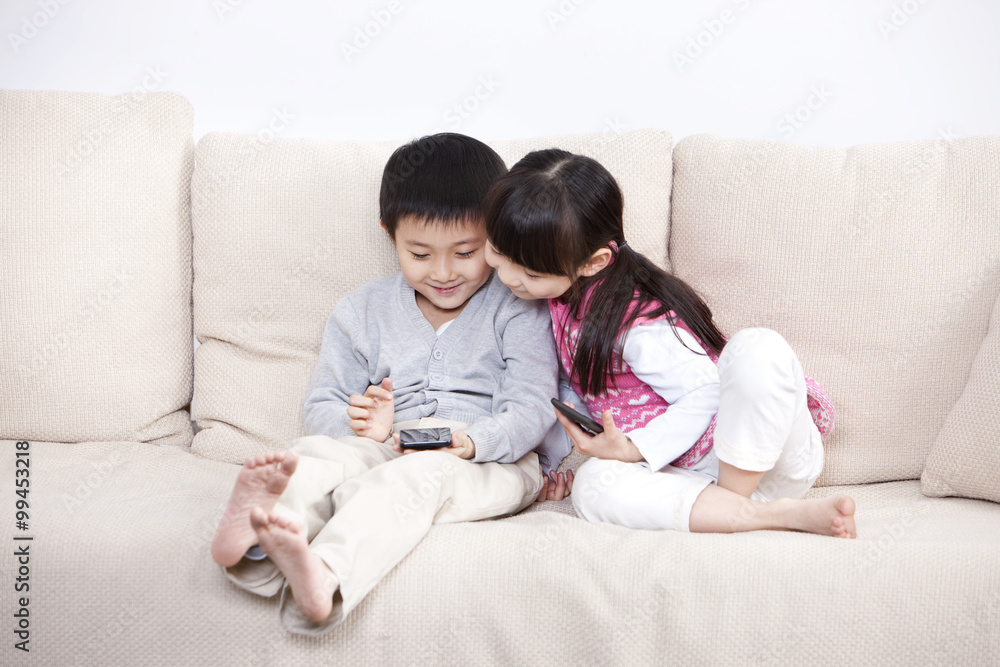 兴奋的男孩和女孩在沙发上玩智能手机