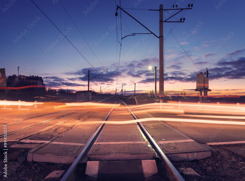 Railroad crossing with car lights in motion at night