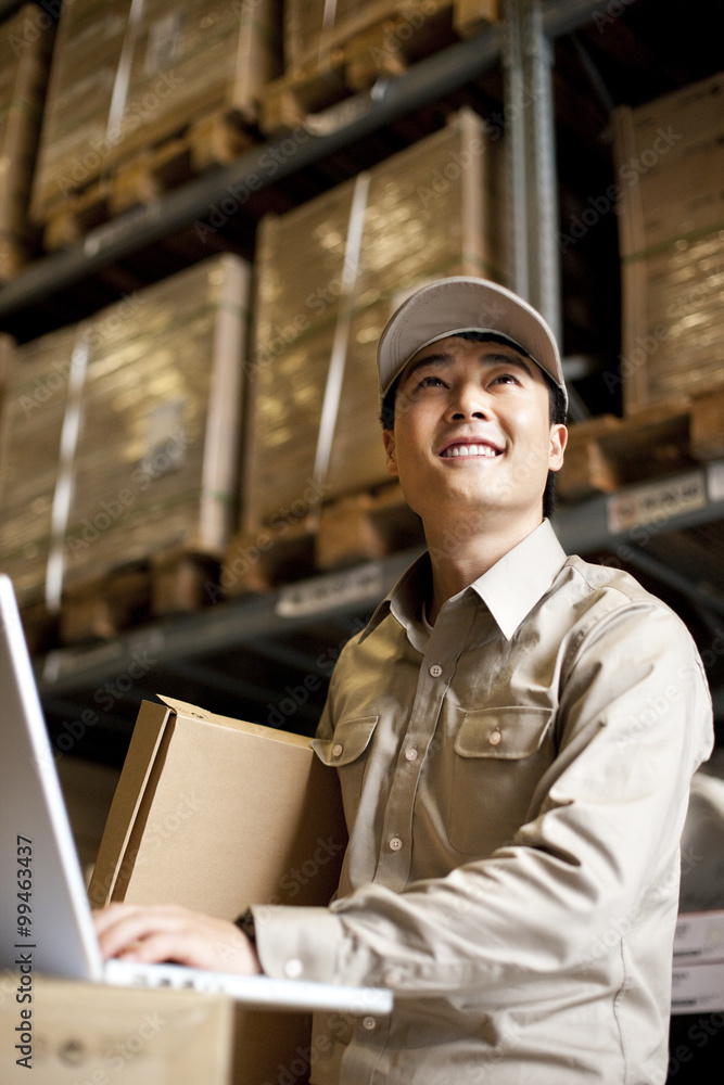 Male Chinese warehouse worker using a laptop